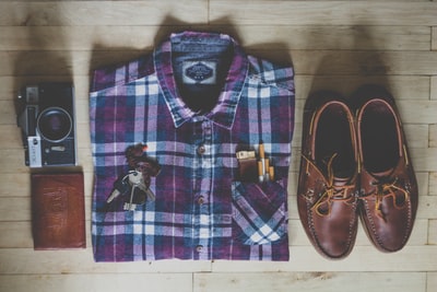 平放摄影的纽扣衬衫，相机，钥匙，香烟，和一双棕色皮革船鞋